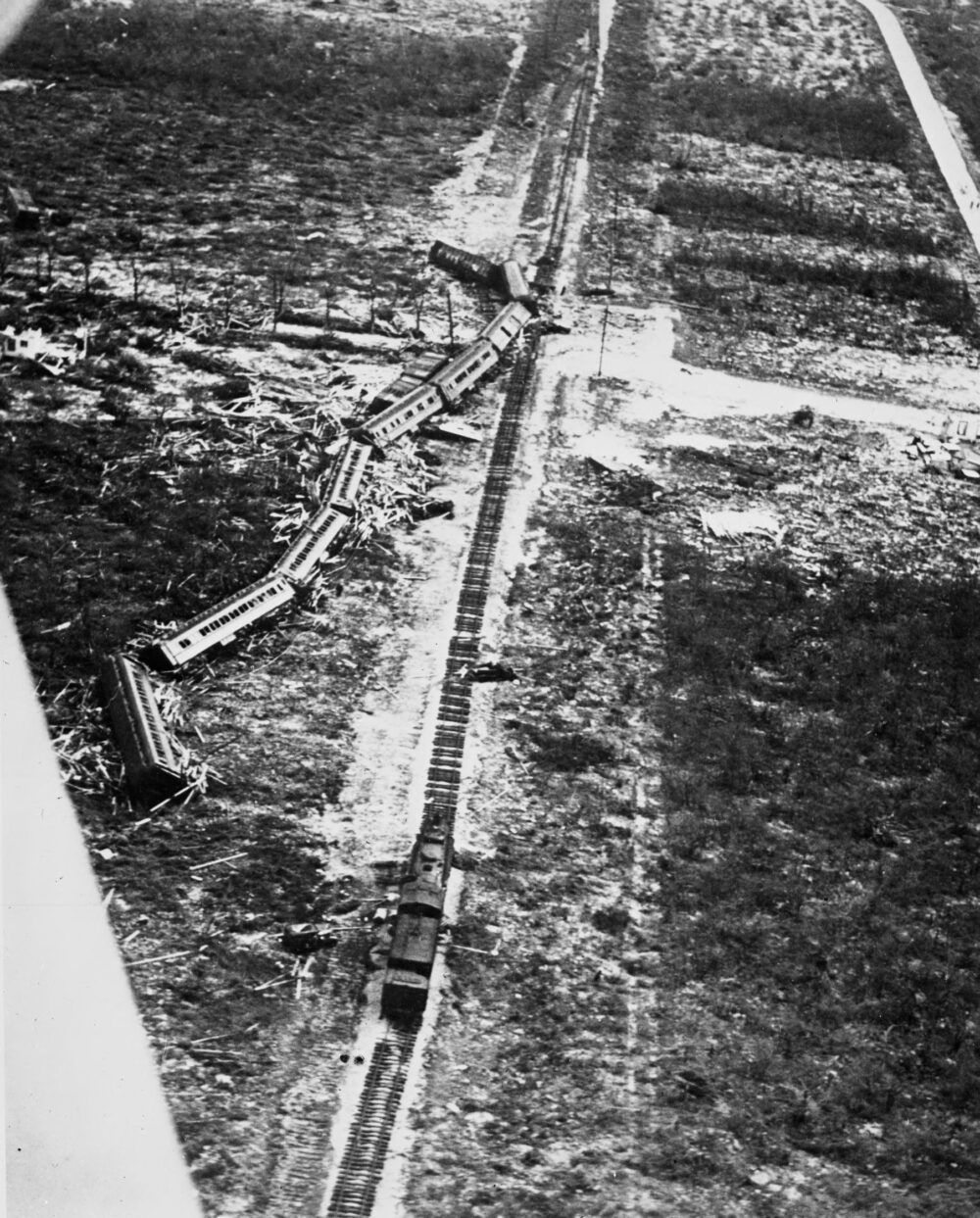 A grainy black and white image of a train crash next to a track, in an empty field. 