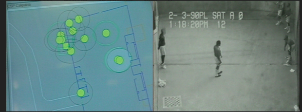 Two-screen video channel. The screen to the left shows green dots on a blue background, appearing to correspond to people in a building or other space. The right screen features CCTV footage of what appear to be dark-skinned men in an indeterminate space, the video is time-stamped "2-3-90PL SAT A 0 1:18:20PM 12"
