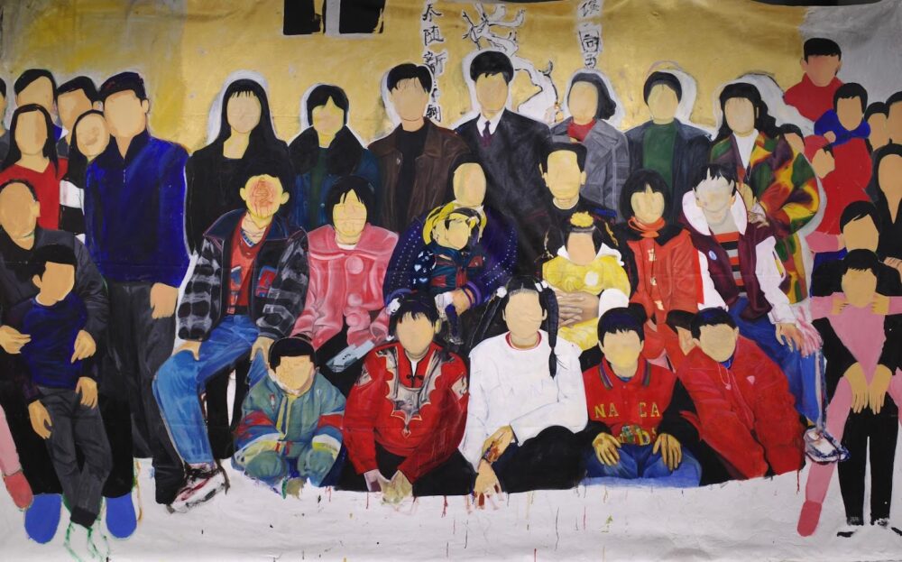 Several rows of people, about thirty-three in total, sit and stand together facing us. They are missing faces but have dark hair wear bright jackets and sweaters, and they are a variety of ages. The background is the same color as their blank faces, a dull yellow. 
