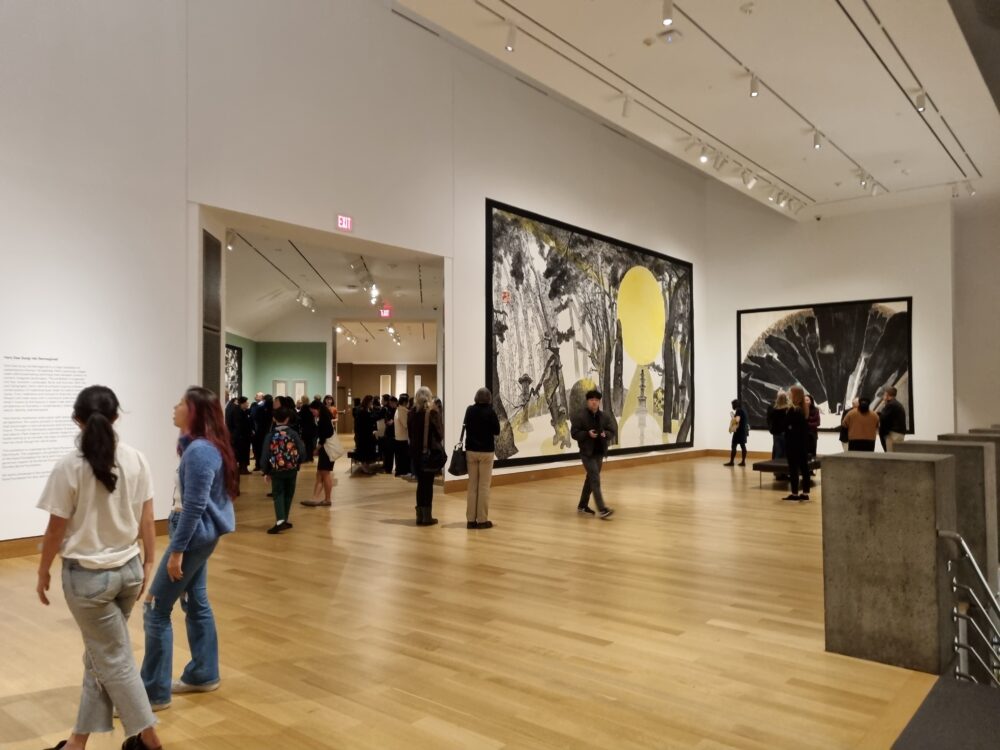 The view of "Park Dae Sung: Ink Reimagined" exhibition at the Hood Museum of Art. Several people walk around on a light wooden floor and view two large paintings hanging on the wall.