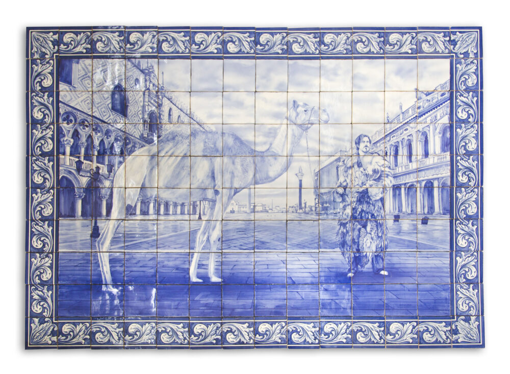 A grid of cobalt blue and white tiles displays a painted image of the artist wrapped in a chicken feather coat leading a camel on a historic street in Saint Tropez, France.