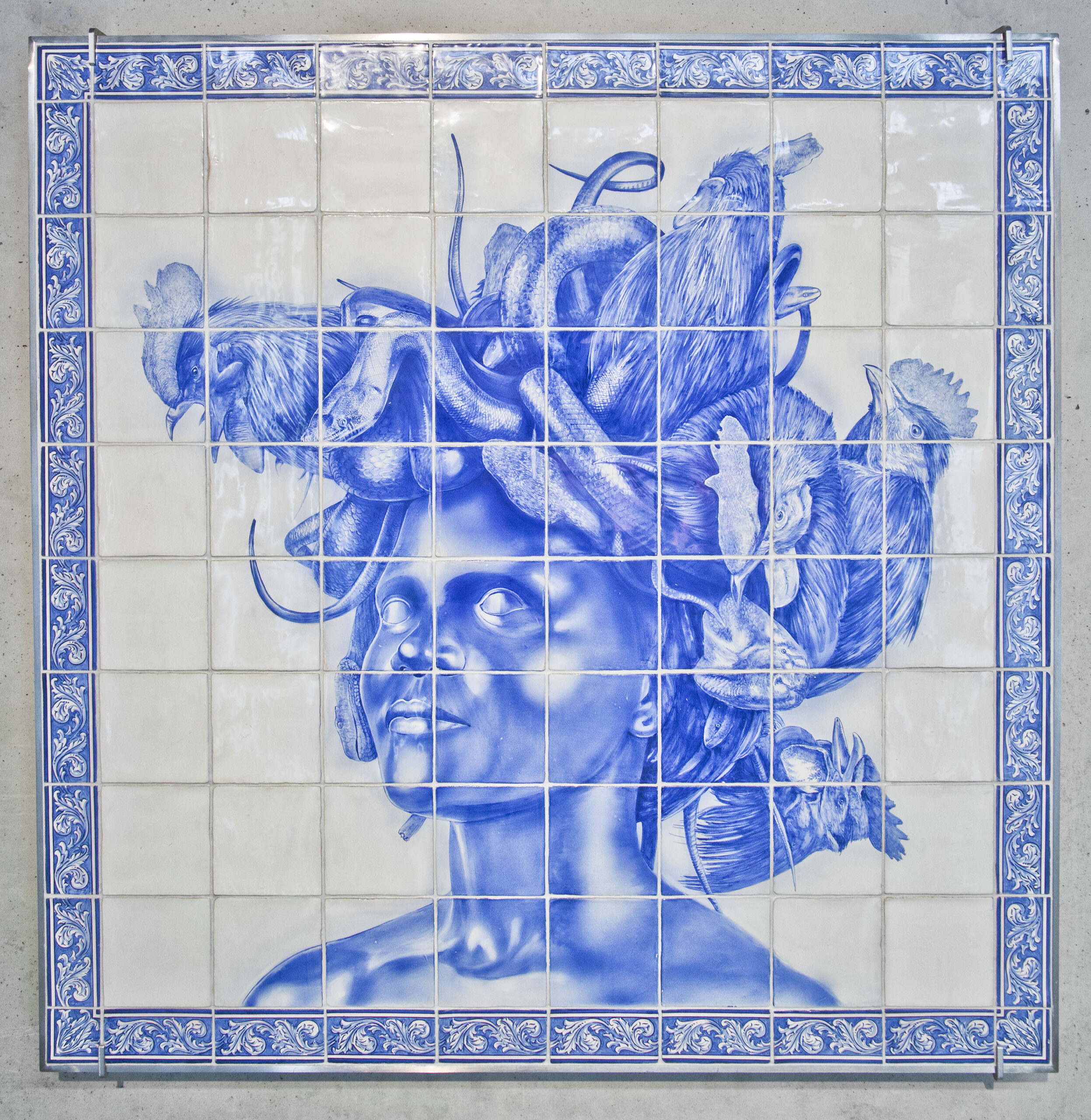 A grid of cobalt blue and white tiles display a painted image of the historic figure Medusa with both snakes and chickens as hair. Her eyes are blank without pupils and stare beyond the edge of the grid.
